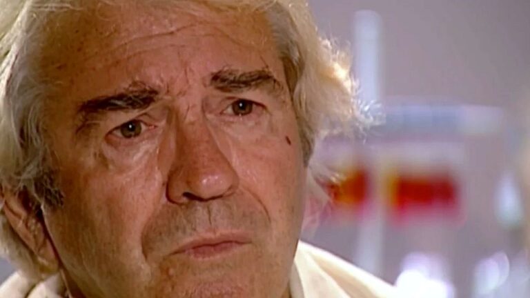 Homem idoso de cabelos grisalhos aparece em close com expressão séria durante entrevista em ambiente interno