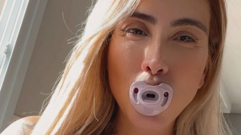 Juju Ferrari aparece em close com chupeta na boca iluminada por luz natural próxima a janela em ambiente interno