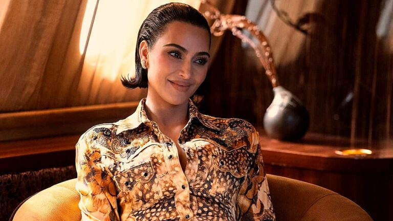 Mulher elegante sorri sentada em poltrona em ambiente sofisticado com decoração ao fundo em cena de série