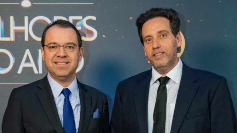 Mário Teixeira e Allan Fiterman posam juntos usando ternos escuros, Mário à esquerda usa óculos e gravata azul, Allan à direita usa gravata preta clara