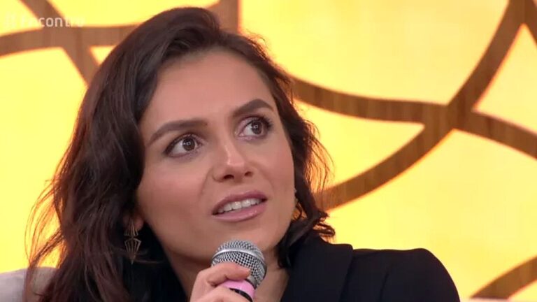 Mulher segura microfone durante participação no programa Encontro com cenário amarelo ao fundo