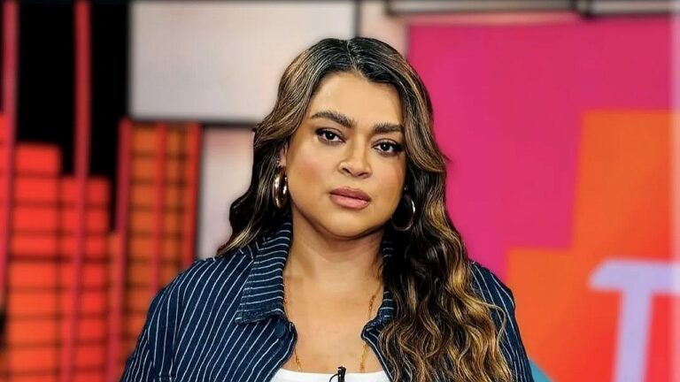 Mulher fala com expressão séria durante participação em programa de televisão em estúdio com cenário colorido ao fundo