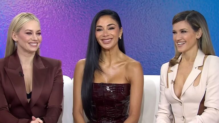 Três mulheres sorrindo participam de entrevista em estúdio de TV sentadas em sofá com fundo colorido