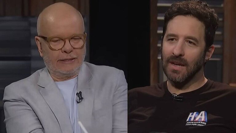 Dois homens conversam durante entrevista em programa de televisão em estúdio com iluminação baixa e cenário de talk show ao fundo