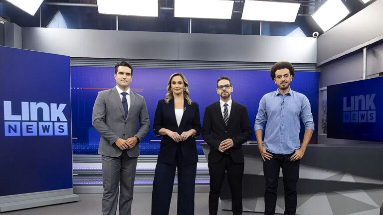 Apresentadores do Link News posam no estúdio do programa com telões e iluminação profissional ao fundo