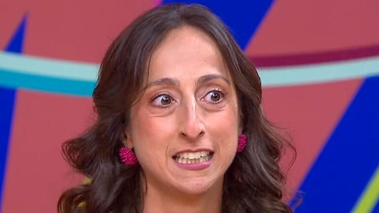 Mulher com expressão tensa participa de programa de TV em estúdio com cenário colorido ao fundo