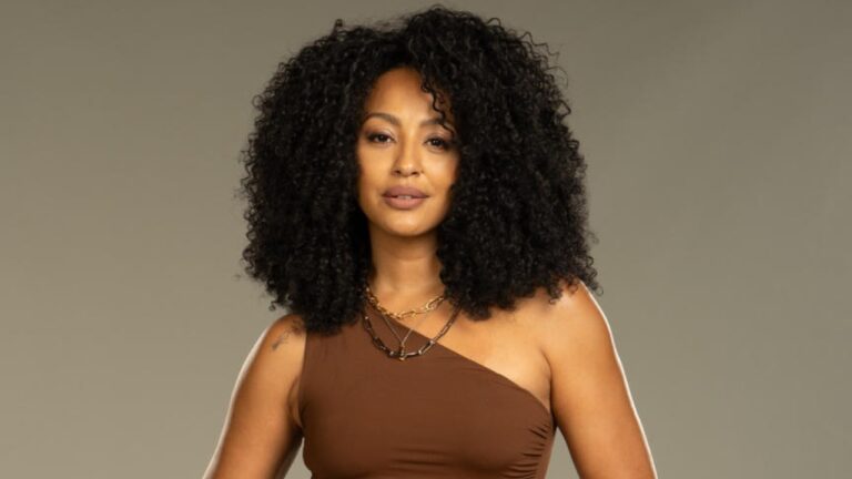 Sheron Menezzes posa com cabelo cacheado volumoso e blusa de um ombro só em fundo neutro de estúdio