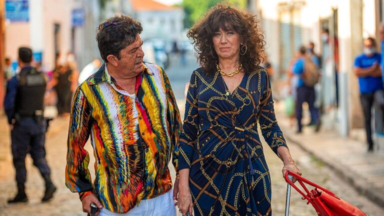 Texto Alternativo disse: Personagens de novela caminham por rua de cidade do interior enquanto conversam em cena gravada ao ar livre