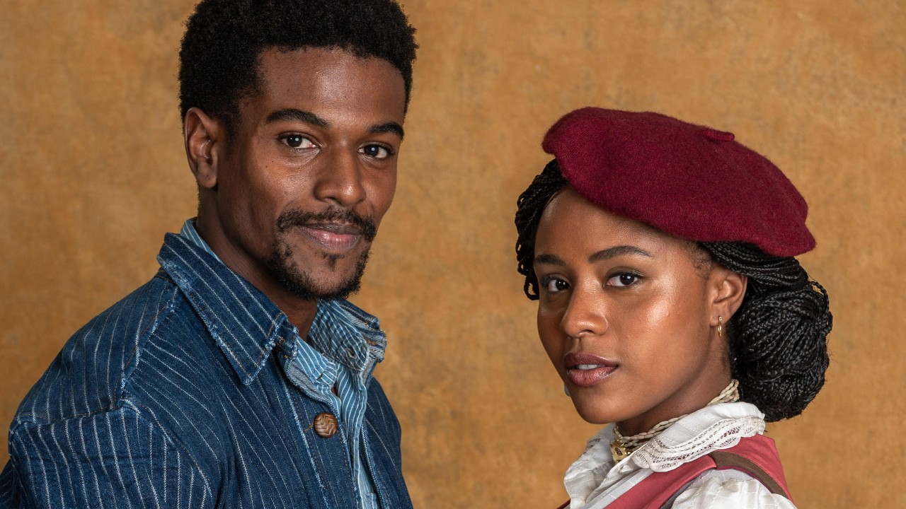 Atores Ronald Sotto e Duda Santos interpretam Tonho e Lúcia na novela A Nobreza do Amor, ele veste jaqueta listrada e ela usa boina bordô sobre fundo bege