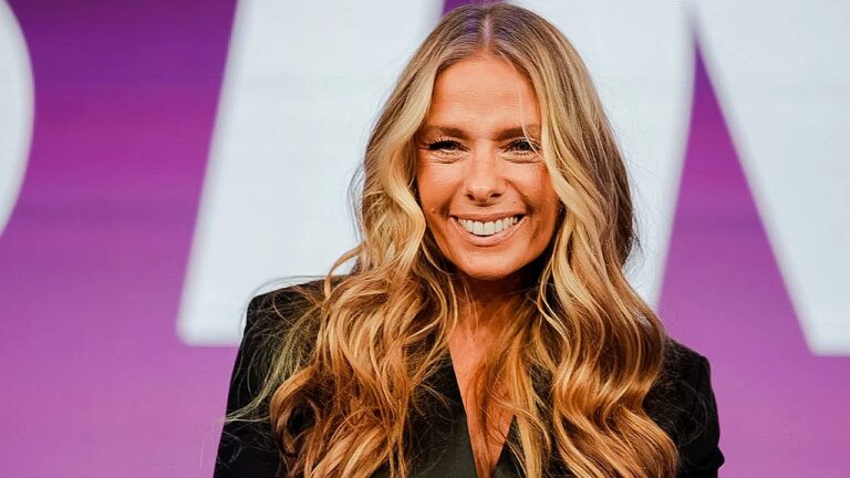 Apresentadora loira sorri em estúdio com fundo colorido durante programa de TV