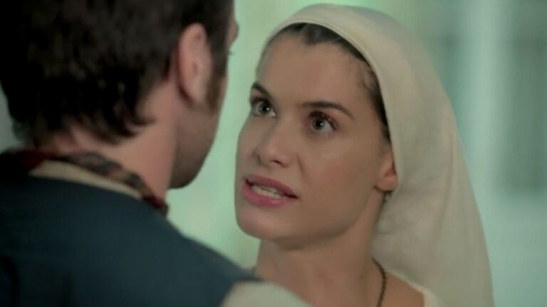 Mulher com véu discute com homem em cena de novela com expressão tensa em diálogo próximo