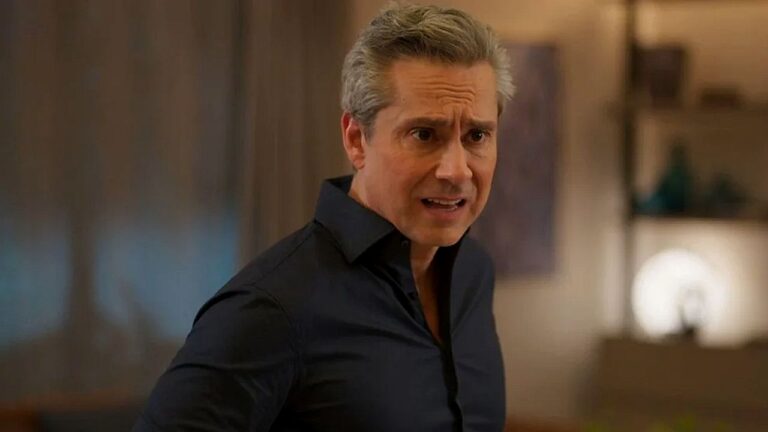 Homem de camisa preta com expressão irritada fala em cena dentro de casa com decoração ao fundo