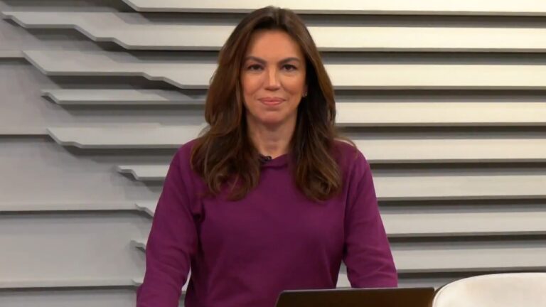 Ana Paula Araújo apresenta jornal em estúdio com bancada e telão de fundo com linhas geométricas