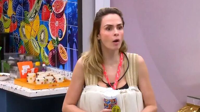 Mulher com crachá reage surpresa em cozinha colorida com frutas na parede e doces sobre a bancada