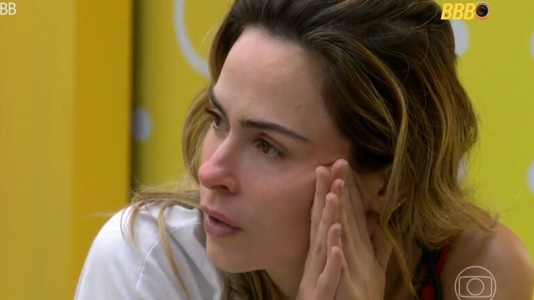 Ana Paula Renault com expressão séria apoia as mãos no rosto durante conversa no BBB em ambiente interno com parede amarela ao fundo