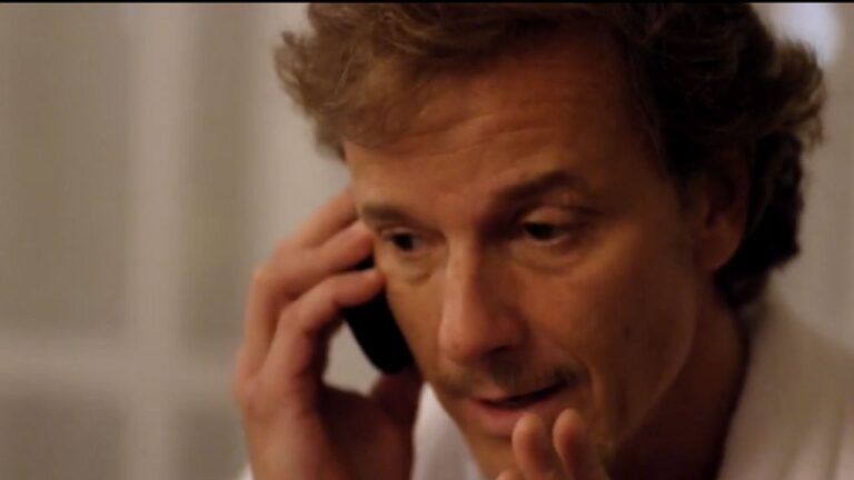 Homem fala ao celular com expressão preocupada em cena ambientada em interior com iluminação suave