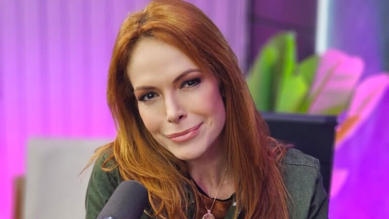 Babi Xavier com cabelo ruivo inclina a cabeça e sorri levemente diante de microfone em estúdio com iluminação colorida ao fundo