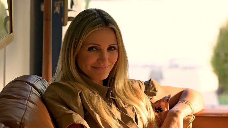 Mulher loira sentada no sofá sorri em ambiente interno iluminado pela luz do sol