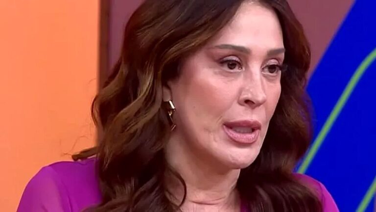 Mulher fala com expressão séria durante participação em programa de TV em estúdio colorido