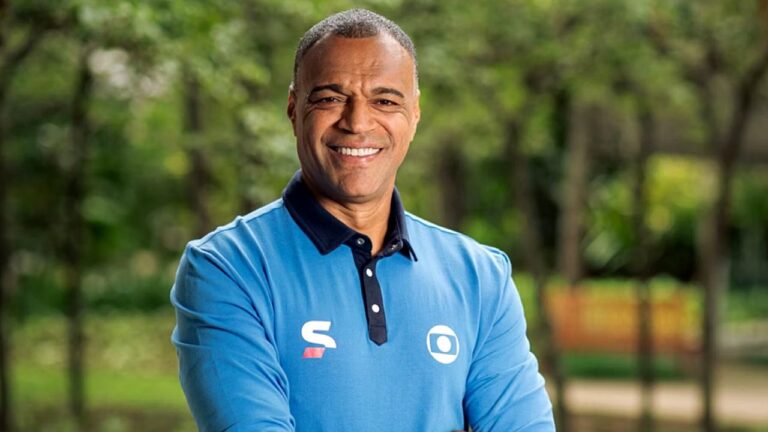 Apresentador esportivo Denilson sorri em foto promocional da TV Globo ao ar livre