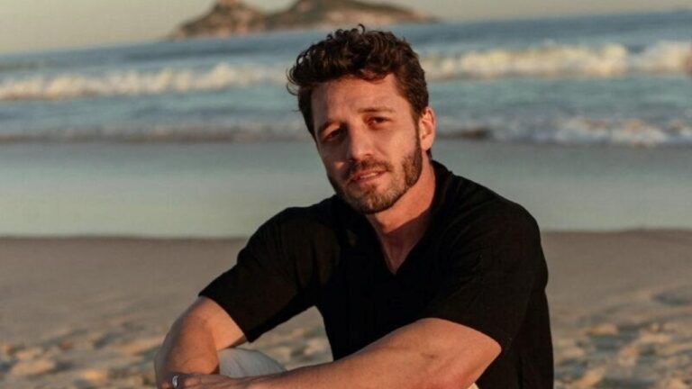 Diogo Venturieri sentado na areia da praia com mar ao fundo durante pôr do sol em ensaio ao ar livre