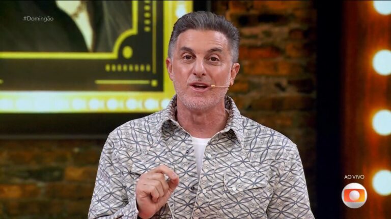 Luciano Huck fala com microfone do estilo headset durante o Domingão, exibido ao vivo na TV Globo, em cenário com telão iluminado.