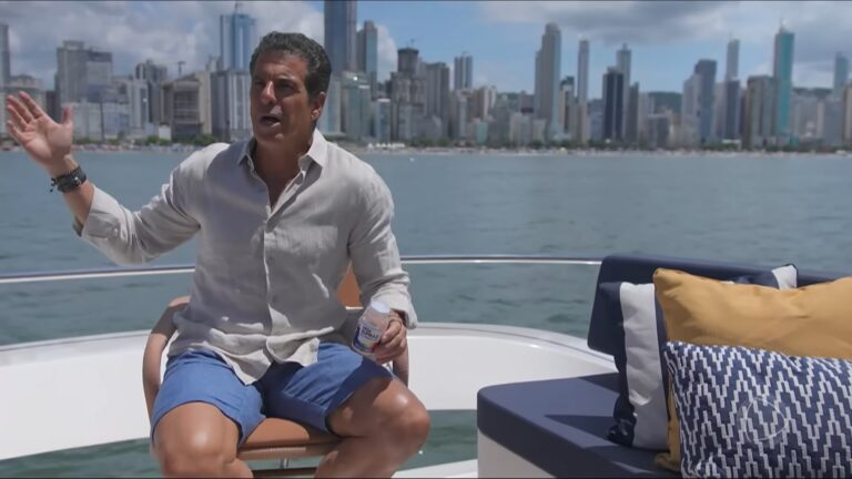 Alvaro Garnero, apresentador do 50 por 1, gesticula sentado em barco com skyline de Balneário Camboriú ao fundo durante gravação do Domingo Espetacular.
