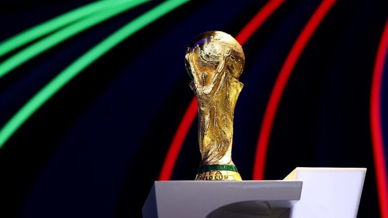 Troféu da Copa do Mundo da FIFA exibido em pedestal com fundo escuro e luzes coloridas em evento oficial