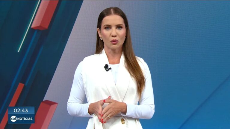 Fabíola Corrêa, apresentadora do SBT Notícias, fala no estúdio vestindo roupa branca, com gráfico ao fundo durante o telejornal.