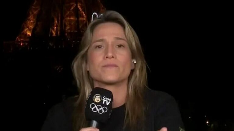 Repórter da CazéTV segura microfone com logo das Olimpíadas durante transmissão noturna em frente à Torre Eiffel