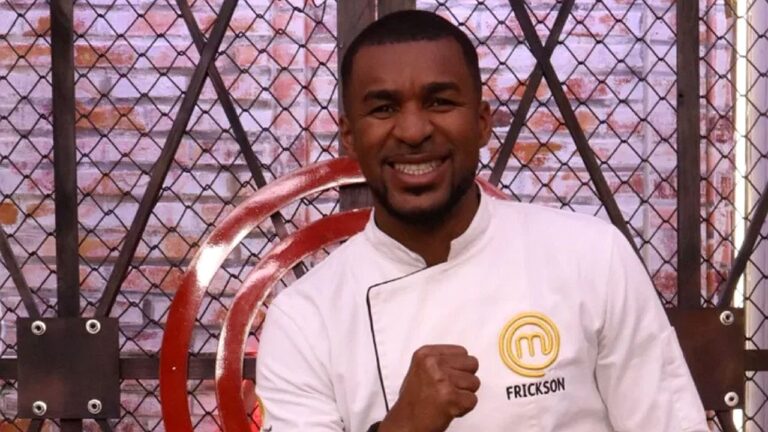 Participante Frickson do MasterChef sorri e faz gesto de comemoração com punho fechado diante do cenário do programa