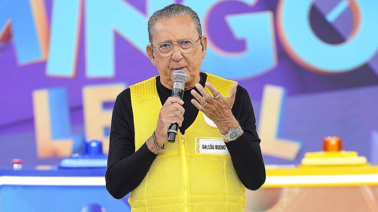 Galvão Bueno fala ao microfone com colete amarelo em participação no programa Domingo Legal