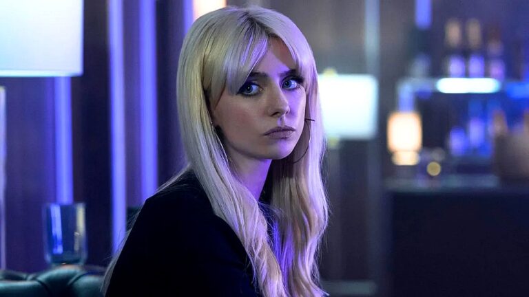 Mulher loira com expressão séria em ambiente com luz azul em cena de série ambientada em bar ou lounge