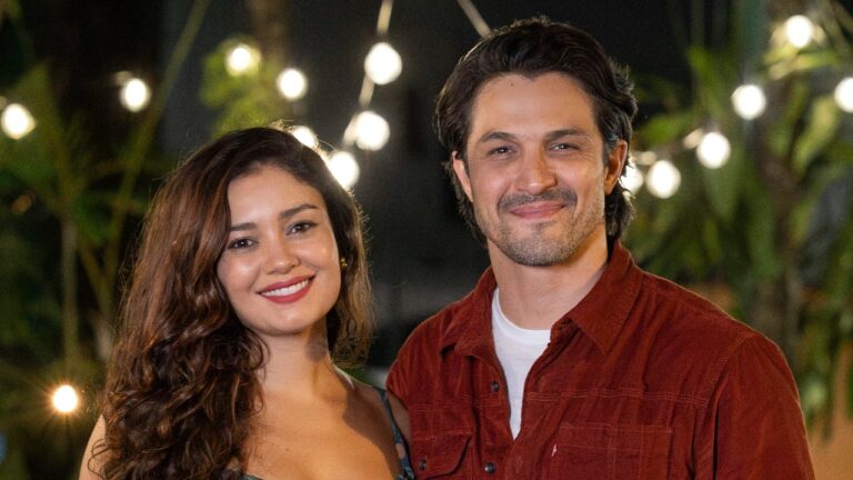 Gerluce (Sophie Charlotte) e Paulinho (Romulo Estrela) sorrindo juntos em cena da novela Três Graças com luzes ao fundo