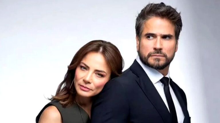 Casal elegante posa junto em foto promocional com homem de terno e mulher apoiada em seu ombro olhando para a câmera