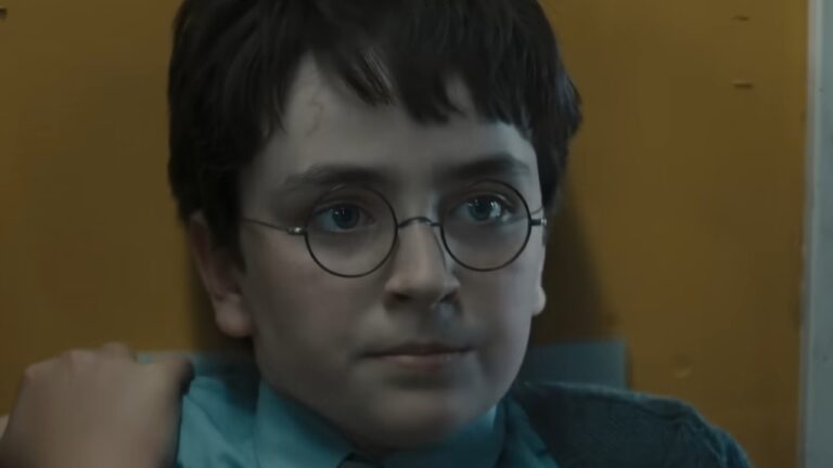 Dominic McLaughlin como Harry Potter aparece de óculos redondos com expressão séria em ambiente interno com parede amarela ao fundo
