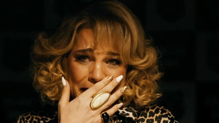 Mulher com lágrimas nos olhos cobre a boca com a mão em cena dramática com fundo escuro