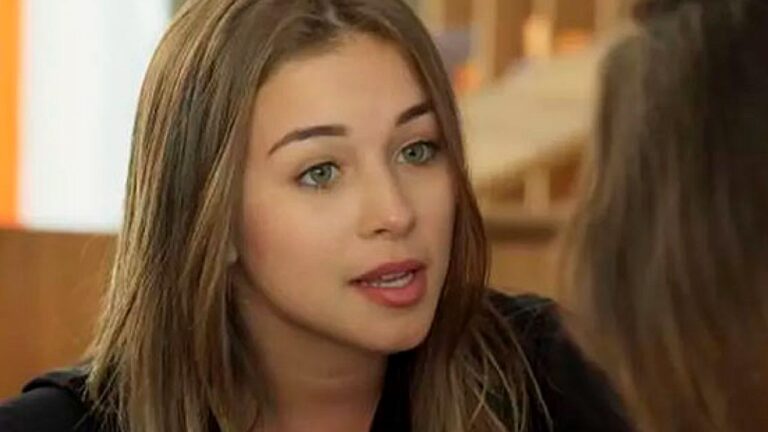 Jovem conversa com outra pessoa em cena de novela com expressão séria em ambiente interno