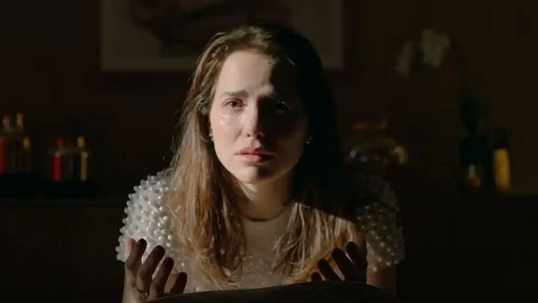 Mulher chora com lágrimas no rosto enquanto encara alguém em cena dramática de novela em ambiente escuro