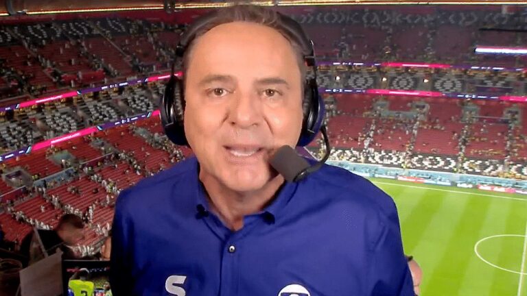 Narrador esportivo com headset transmite jogo de futebol direto de estádio com arquibancadas ao fundo