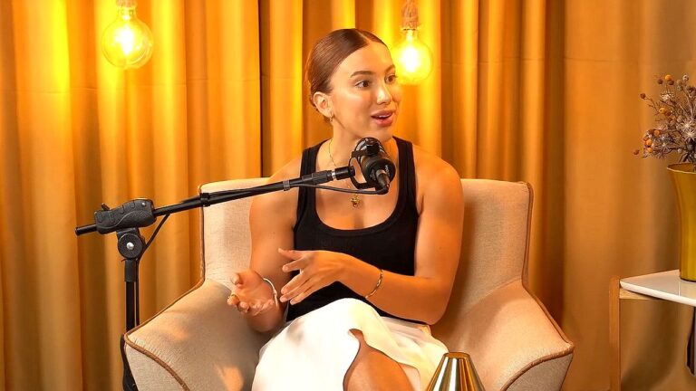 Mulher participa de podcast com microfone em estúdio iluminado com luzes decorativas ao fundo