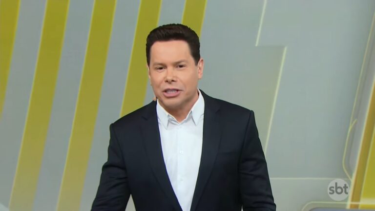 Marcão do Povo, apresentador do Primeiro Impacto, veste terno preto e fala no estúdio com fundo de linhas amarelas e logotipo da emissora.