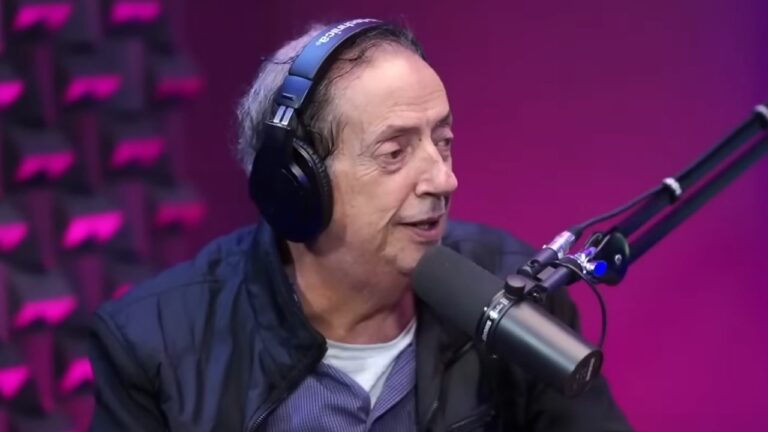 Marcos Oliveira usa fones de ouvido e fala ao microfone em estúdio de podcast com iluminação rosa ao fundo