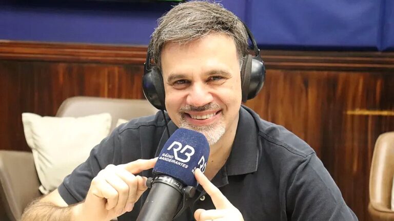 Apresentador com fones de ouvido fala ao microfone da Rádio Bandeirantes durante programa em estúdio