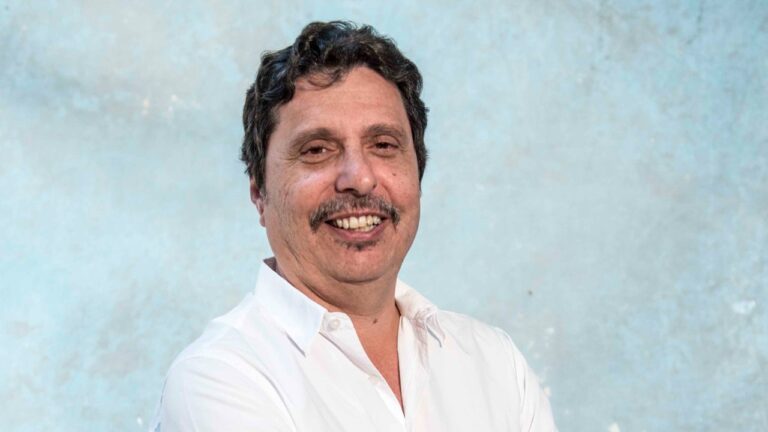 Mauro Wilson sorri usando camisa branca diante de fundo neutro em retrato posado