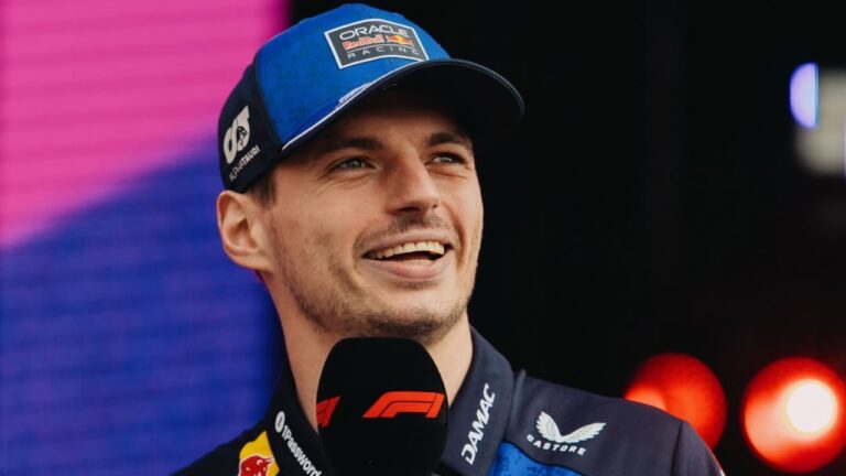 Max Verstappen sorri usando boné da Red Bull e segura microfone da Fórmula 1 durante entrevista em evento esportivo