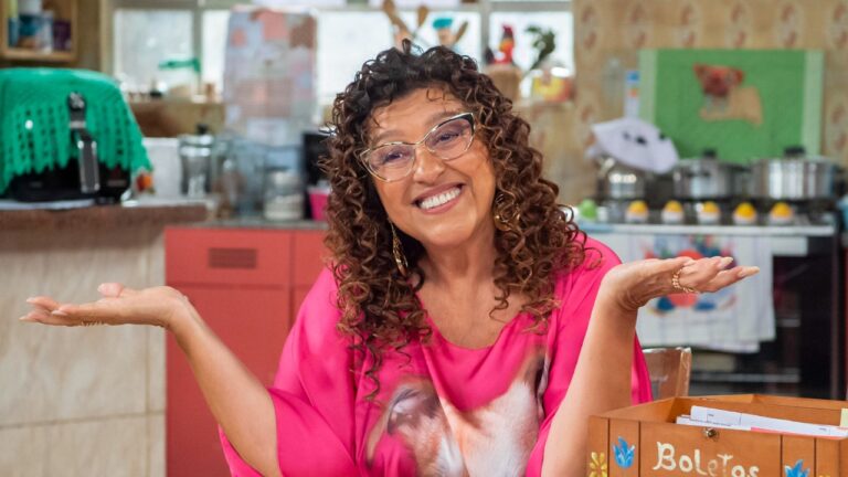 Regina Casé como Mirinda sorri com braços abertos em cozinha colorida durante cena do humorístico Tô Nessa!