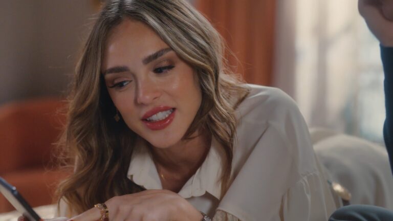 Naiane, interpretada por Isabelle Drummond, observa celular e sorri levemente em cena de Coração Acelerado, novela da TV Globo, ambientada em sala com iluminação aconchegante.