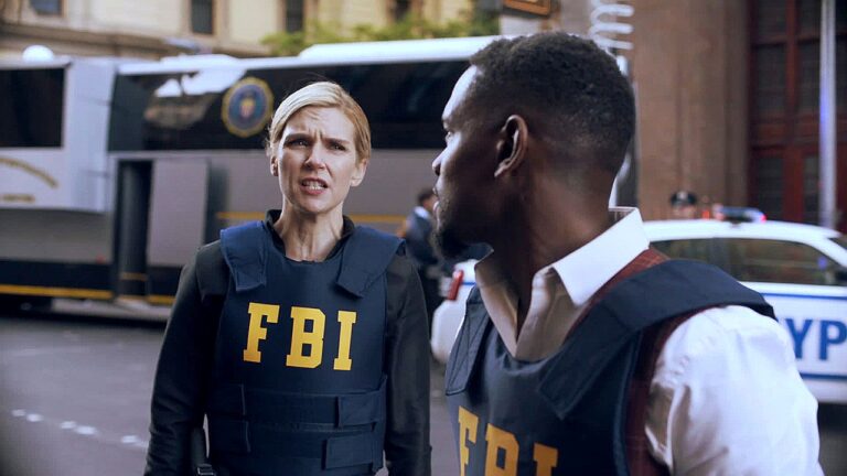 Agentes do FBI com coletes táticos conversam em rua com viaturas policiais e ônibus ao fundo durante operação