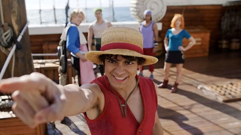 Personagem com chapéu de palha aponta à frente em cena do live-action de One Piece com tripulação ao fundo no navio